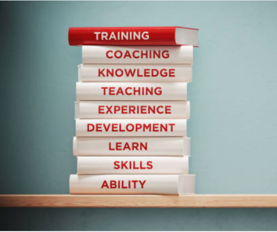 A stack of books with the following words on their spines; training, coaching,knowledge, teaching, experience, development, learn, skills, ability