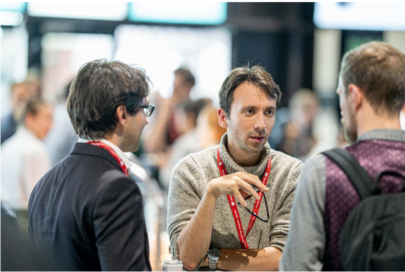 Three men talking to each other at an event, they are all standing, in a crowded room