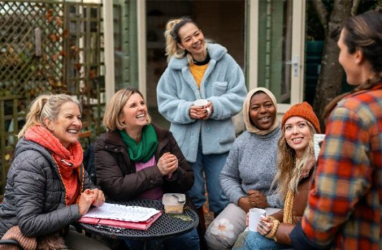 A group of women outside. They are dressed warmly and holding mugs of tea.