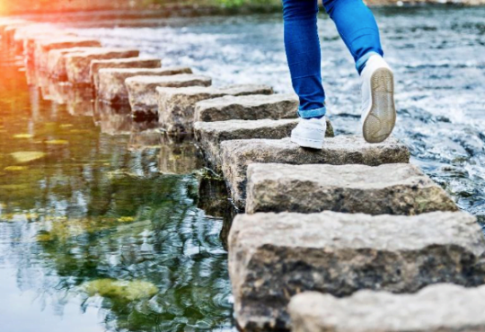 A person from the knees down, walking over stepping stones in water