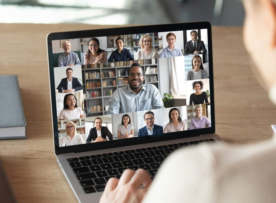 Decorative image: a person looking at a laptop screen which shows a large number of colleagues on a video call
