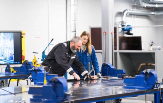 MoD -Decorative image: Two colleagues working together in a workshop, wearing coveralls.
