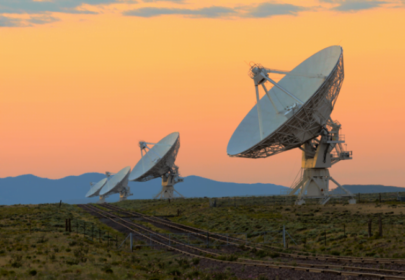 Decorative image: a row of large satellite dishes on the ground, pointing to an evening sky, at sunset