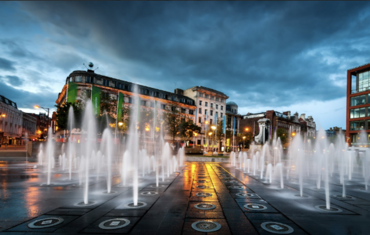 Piccadilly Square in Manchester, at twilight. There are lit water fountains in the foreground.