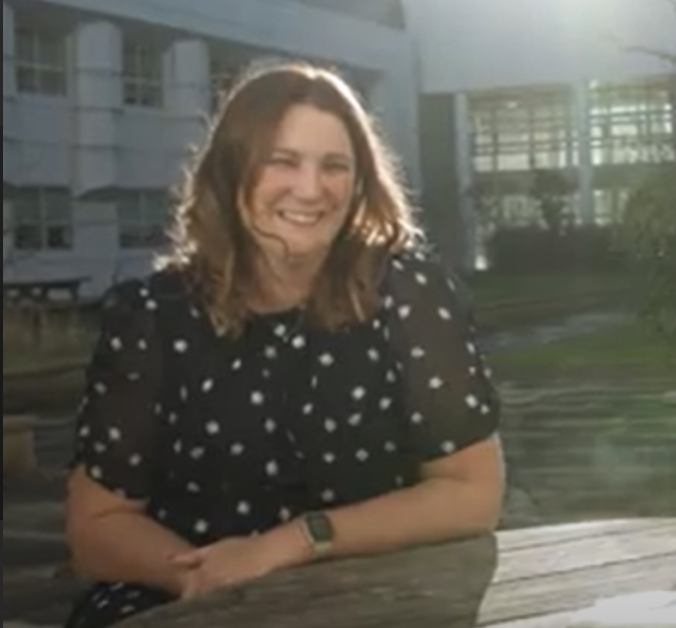 Alex Morley. She is sitting outside at a picnic bench. The sun is shining.