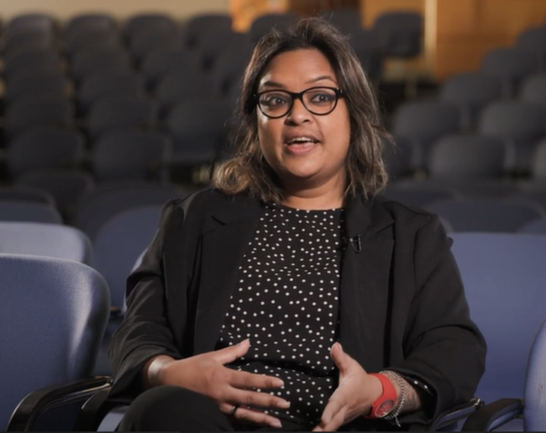 Ghaitree Mungroo. She is sitting in an auditorium, speaking animatedly, and is wearing a striking red watch