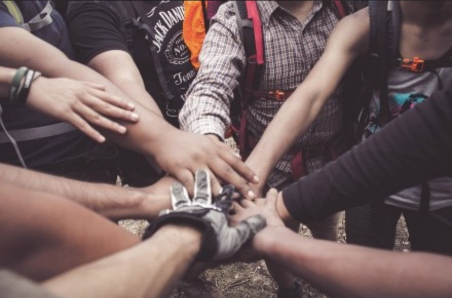 A group of people in hiking attire standing in a circle and touching hands in the middle