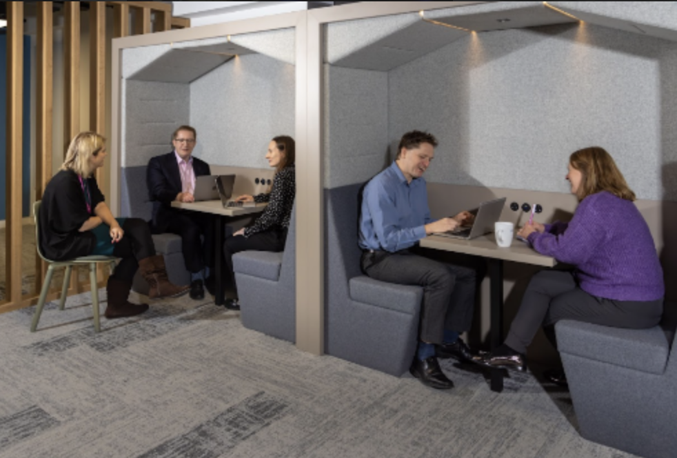 Colleagues working in pods, with comfortable chairs and shared tables.