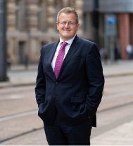 Mark Chivers, Government Chief Property Officer Director General. He is pictured from the waist up, wearing a dark blue suit with purple tie. He is smiling.