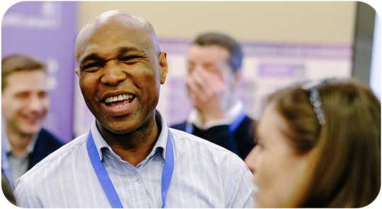 colleagues are gathered around clearly in animated conversation. One man is in focus in the middle of the picture, he is laughing