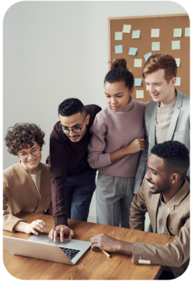 a diverse group of colleagues huddle around a laptop 