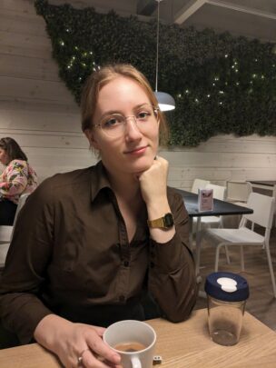 Image of Agnia, sitting at a a table with a coffee, resting her chin on her hand.