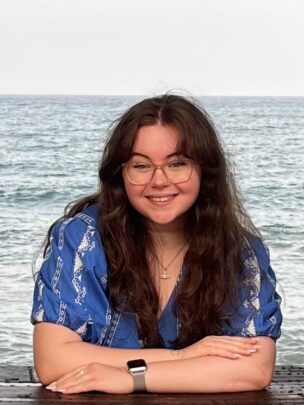 Image of Ella smiling at the camera, with the sea behind her.