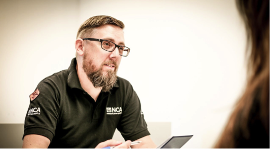 An NCA Operative working at a desk. He is wearing a uniform.