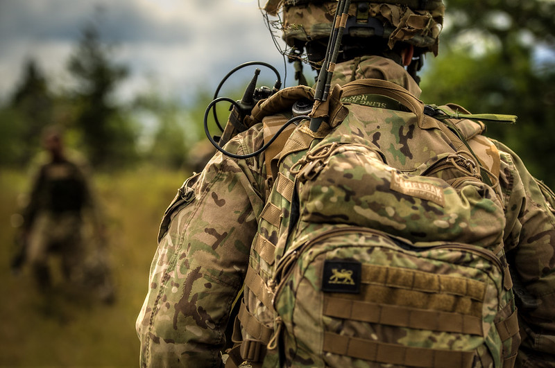 The back view of a soldier in the field in uniform and carrying a backpack.
