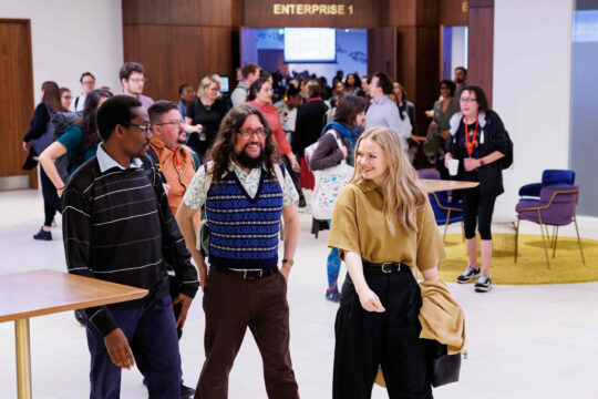 Decorative image: Three (3) causally dressed colleagues, walking through a workspace together