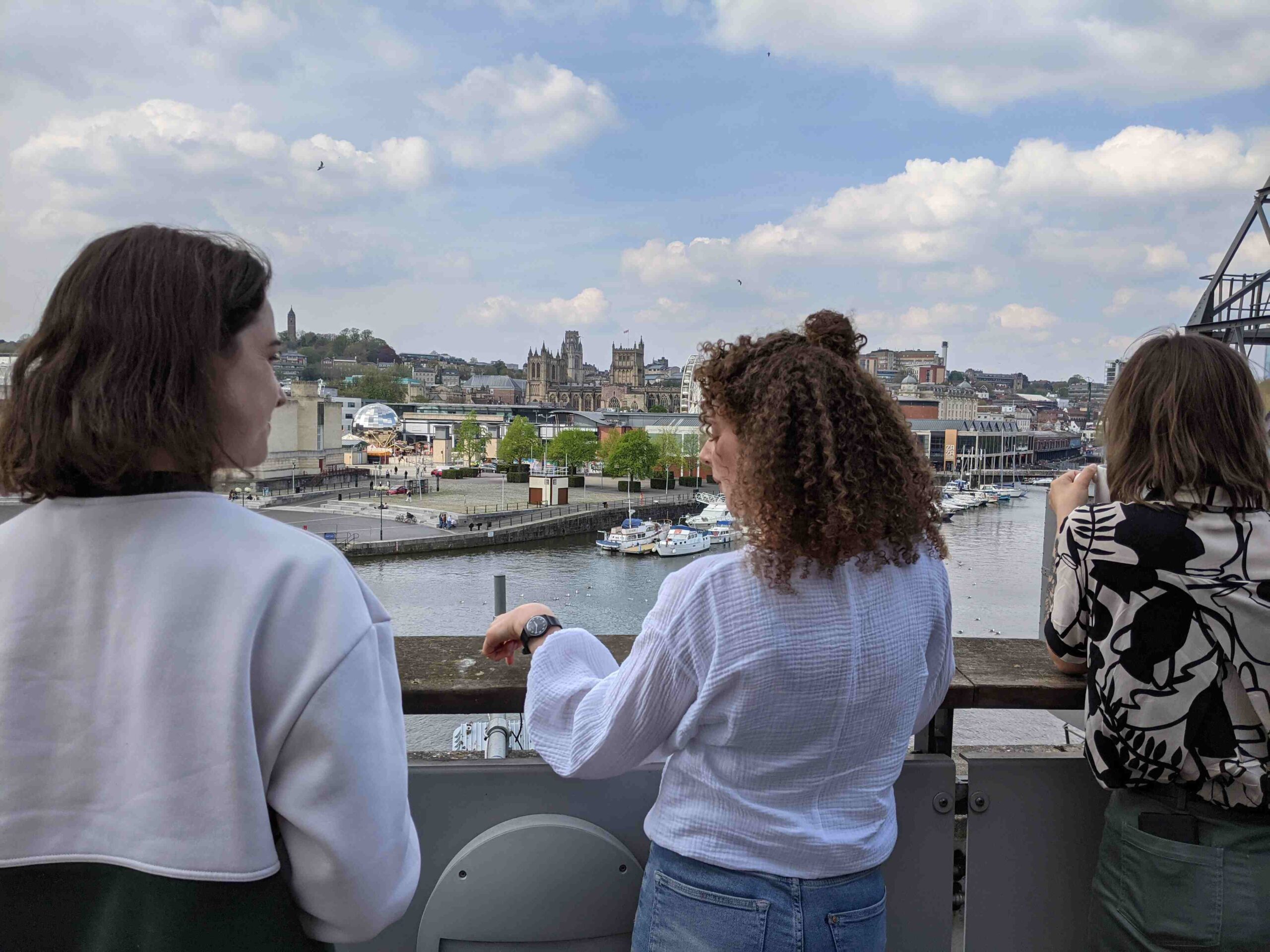 Decorative image: three (3) people standing on a balcony together, looking over a river and city skyline