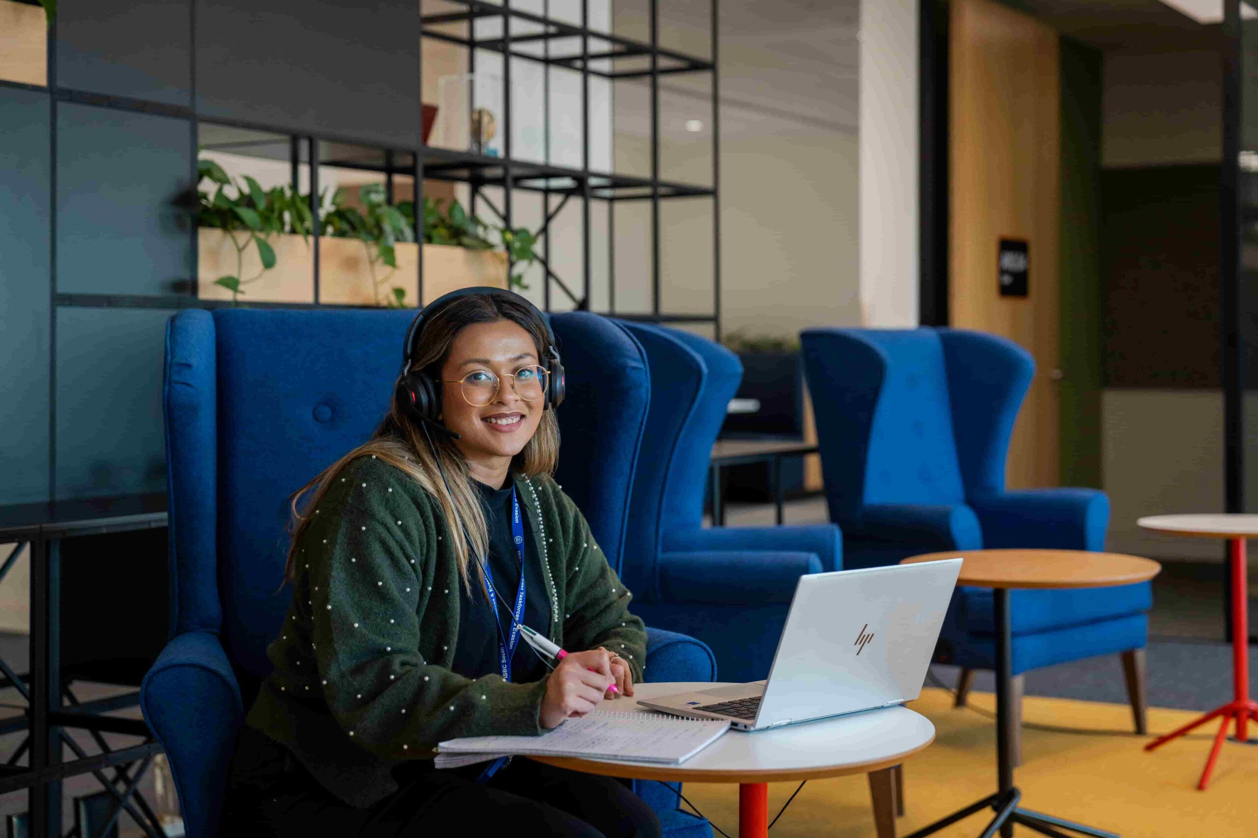 woman sat with a laptop wearing a headset smiling at camera