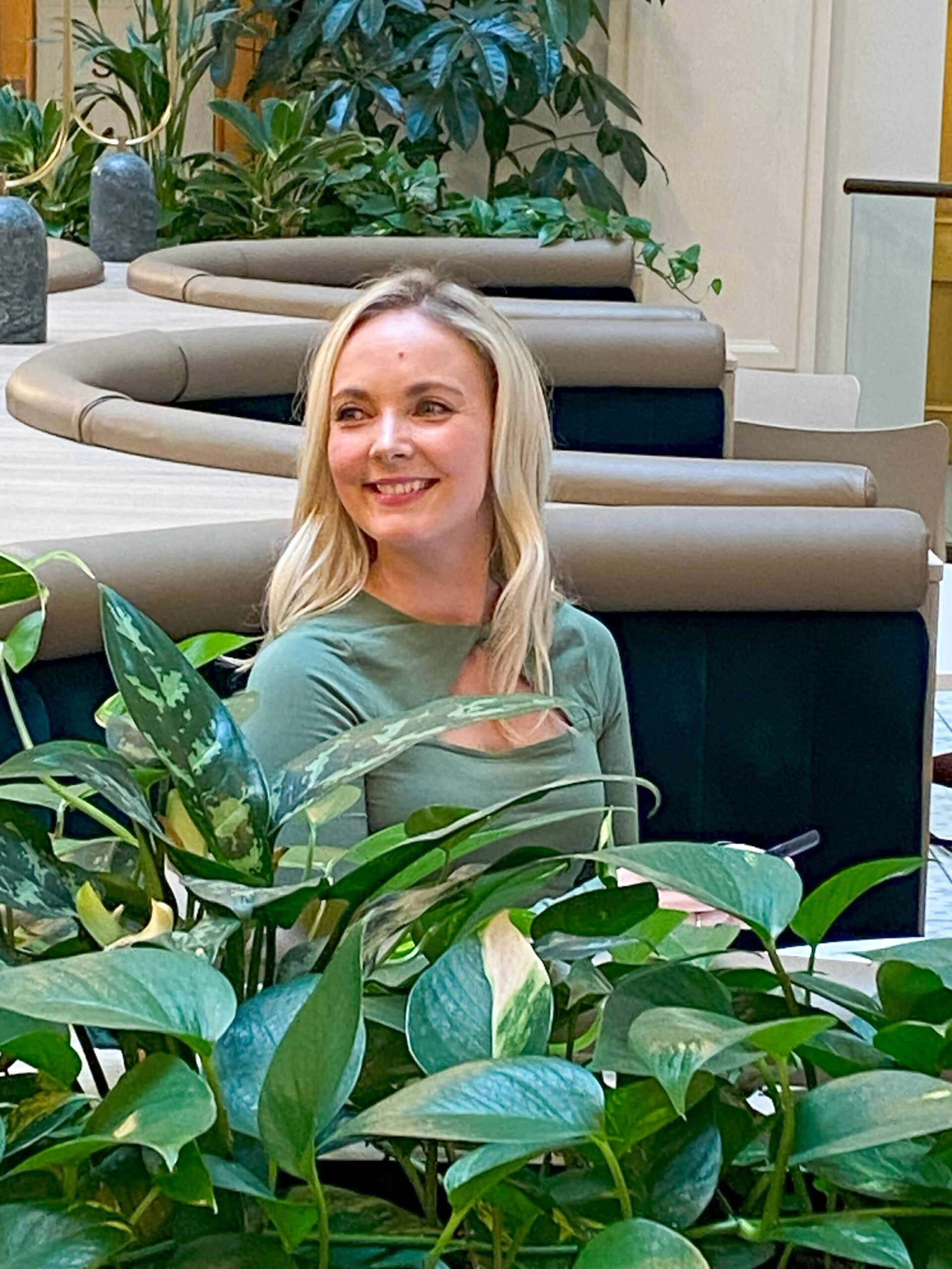 A woman sat behind a plant smiling