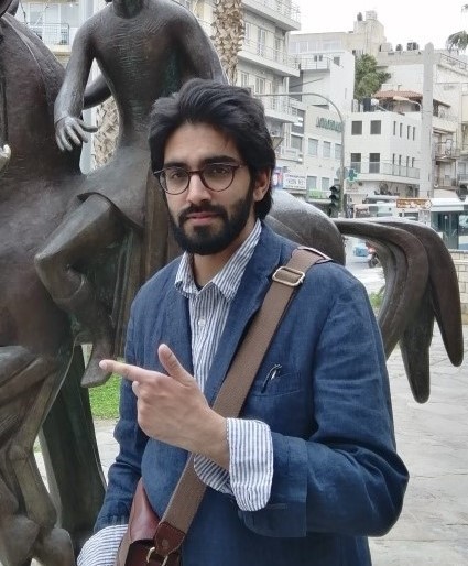 A photo of Zahid. Zahid wearing a bag over his shoulder pointing at a statue