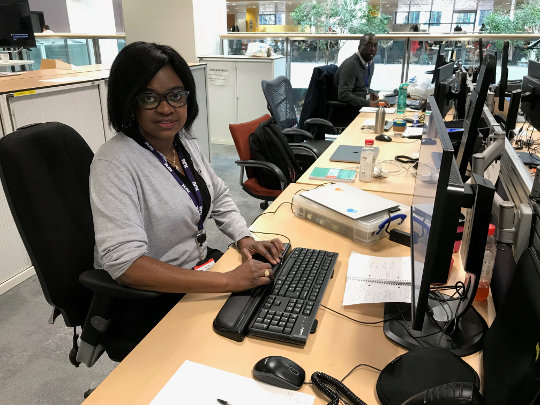 A photo Of A Knowledge And Information Management Team Member, she is sitting at her desk and is dressed in a white shirt