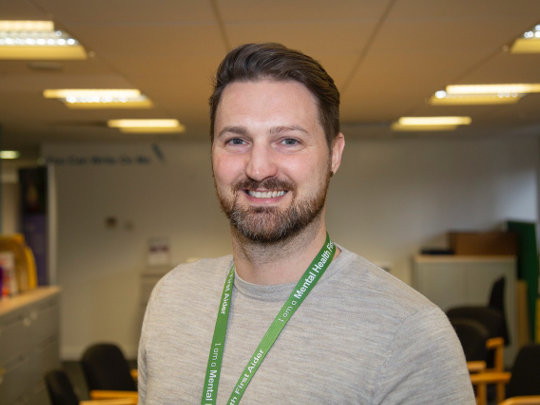 A Portrait photo Of Chris Murray from Department for Work and Pensions. He is smiling and wearing a green mental health first-aider lanyard
