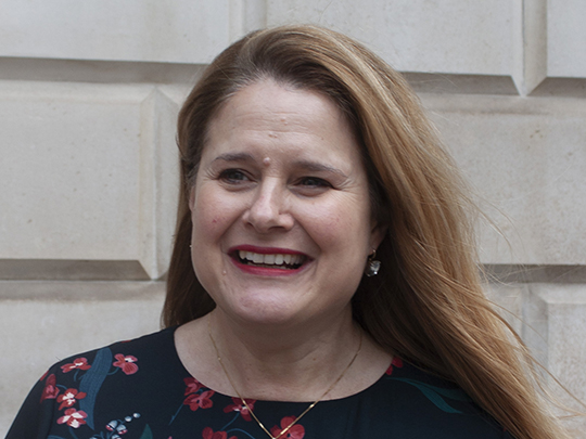 A photo of Katharine (a Senior Policy Adviser in HM Treasury) outside the Treasury building. She has long brown hair and is smiling.