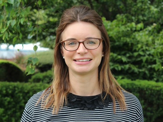 A photo Of Katie Dawson. She has brown hair, in a half-up style and is wearing dark framed glasses and a striped top.