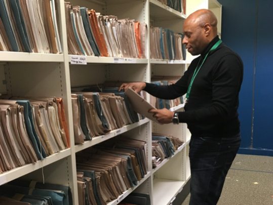A Team Member From The Knowledge And Information Profession, searching through shelves of files to locate something