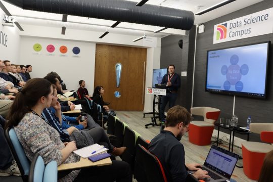 A group of people in a campus lecture room, watching a Data Science presentation.