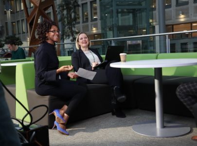 Two women sitting at s table chatting and laughing. They are wearing business wear.