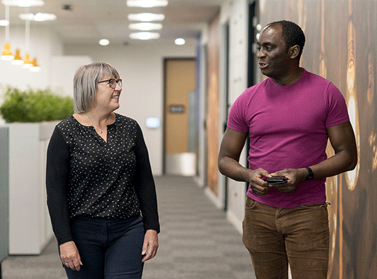 Colleagues walking and chatting along a bright office corridor