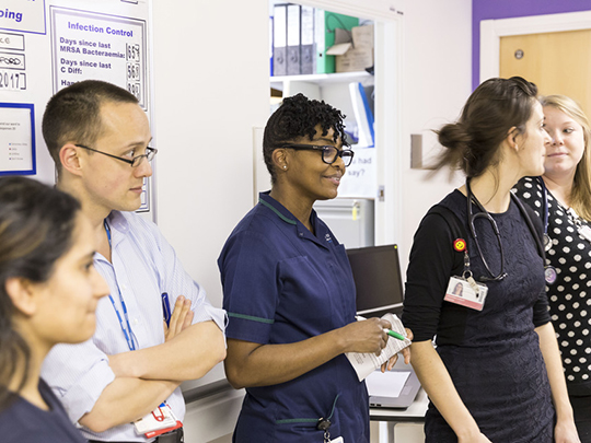 Doctors And Nurses Gathered In Hospital Corridor Meeting At Uclh