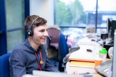 A DVLA team member. He is wearing a headset and speaking on the phone at his desk, which is comfortably cluttered.