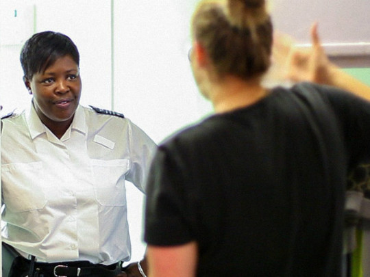 A photo of a female Prison Officer And Offender. The officer is facing the camera, and the offender is facing away.