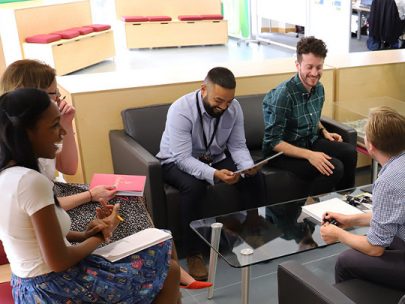 Five Team Members At Homes England. They are sitting in a casual office and chatting together.