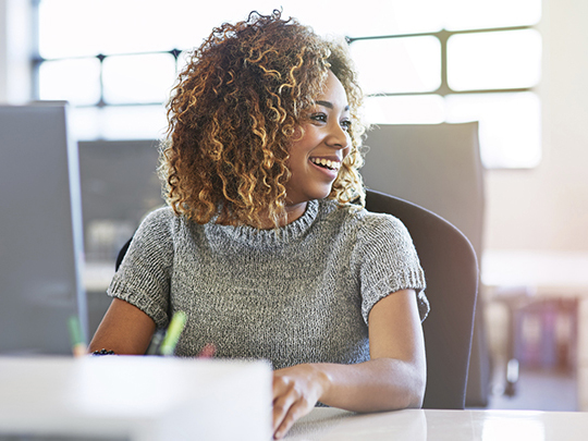 Decorative image: A Commercial Profession team member, sitting at a desk, she is turned to the side, smiling at a colleague out of shot
