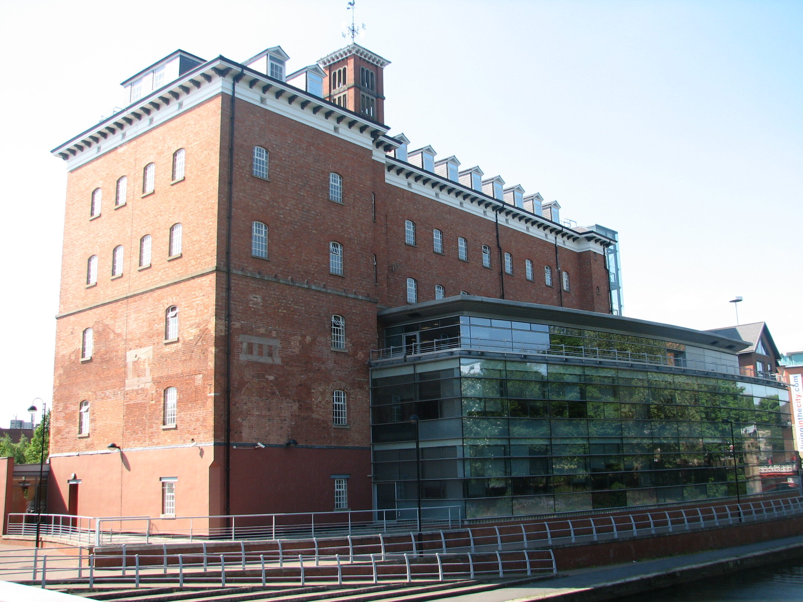 HM Land Registry's Leicester Office, a redbrick Victorian building, with a modern glass fronted extension to the front. The green foliage from the public gardens facing the building, is reflected in the glass of the extension.