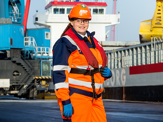A photo of Lucy Walker a Marine Apprentice at DfT, she is wearing fluorescent orange coveralls, and a hardhat.