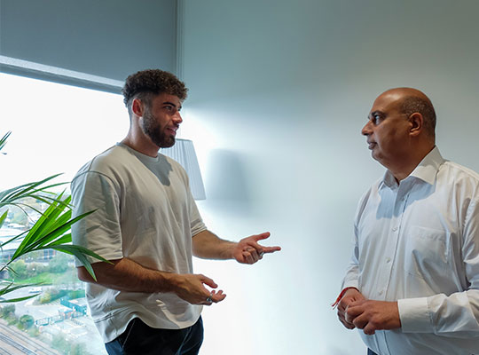 Two male colleagues stood in an office space chatting