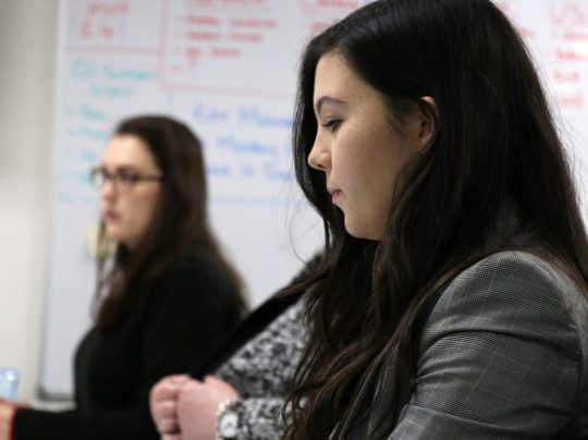 Two Counter Fraud Team Members sitting at their desks. Their is a whiteboard covered in writing in the background.