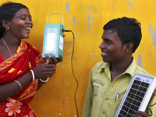 Two People Smiling With Electronic Equipment In Front Of Yellow Wall