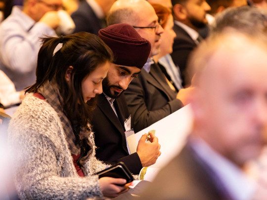 Two Security Profession Team Members sitting together at a conference, reading a booklet.