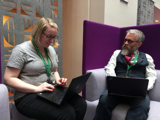 Two Team Members In the Collaboration Knowledge And Information Profession, sitting in comfy purple chairs, working on their laptops
