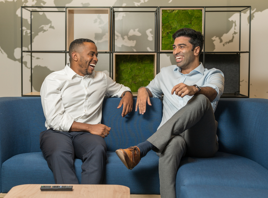 2 colleagues smile and laugh together on a sofa