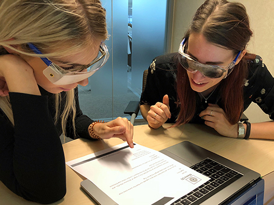 Two colleagues trying out Visual Impairment Simulation Goggles, and viewing a document together