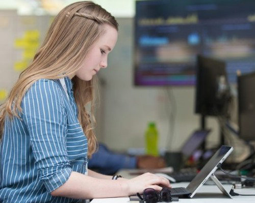 An Operational Delivery team member, working on a laptop. She is wearing a light blue blouse and is in an office environment